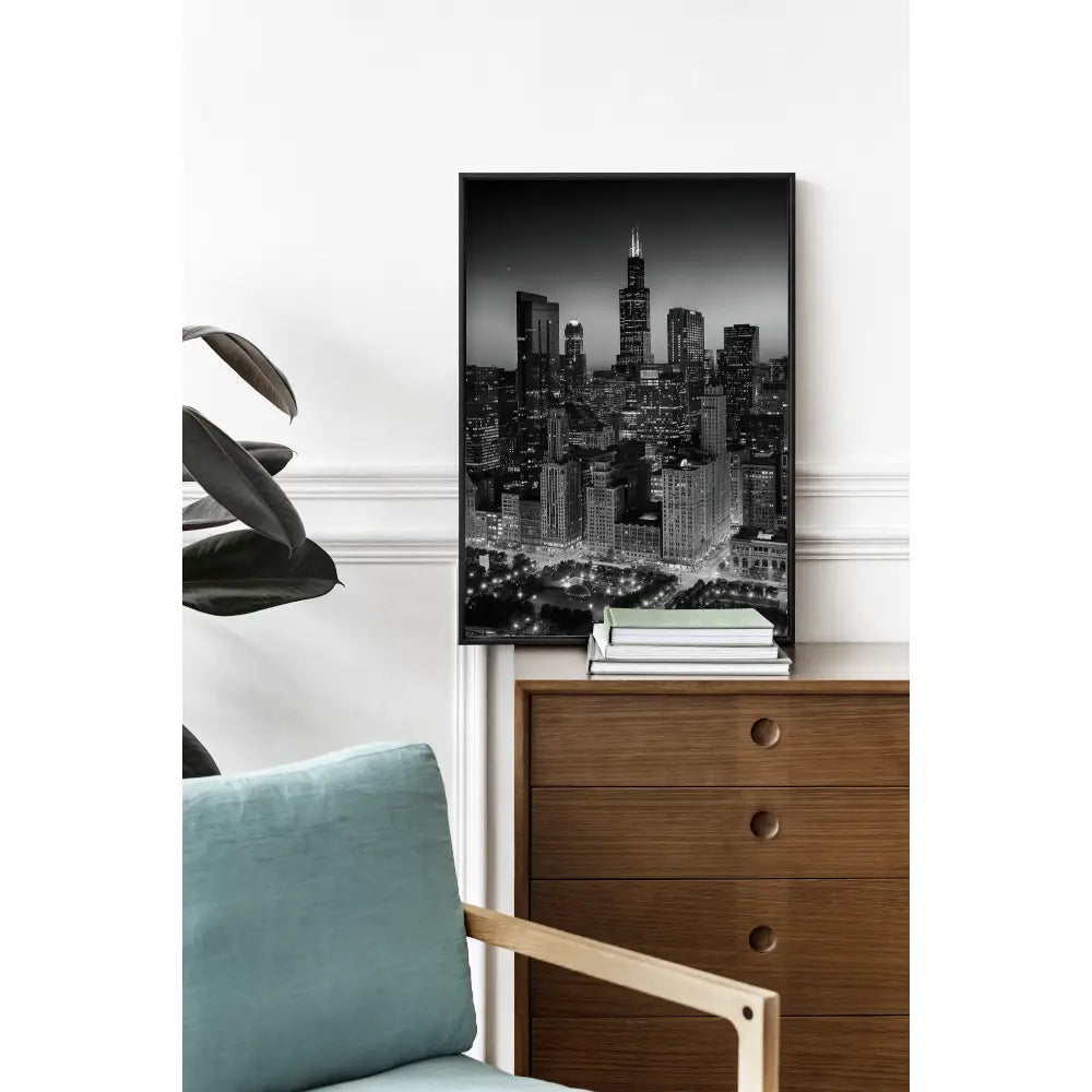 Cityscape artwork on a wall above a wooden dresser with books and a plant.