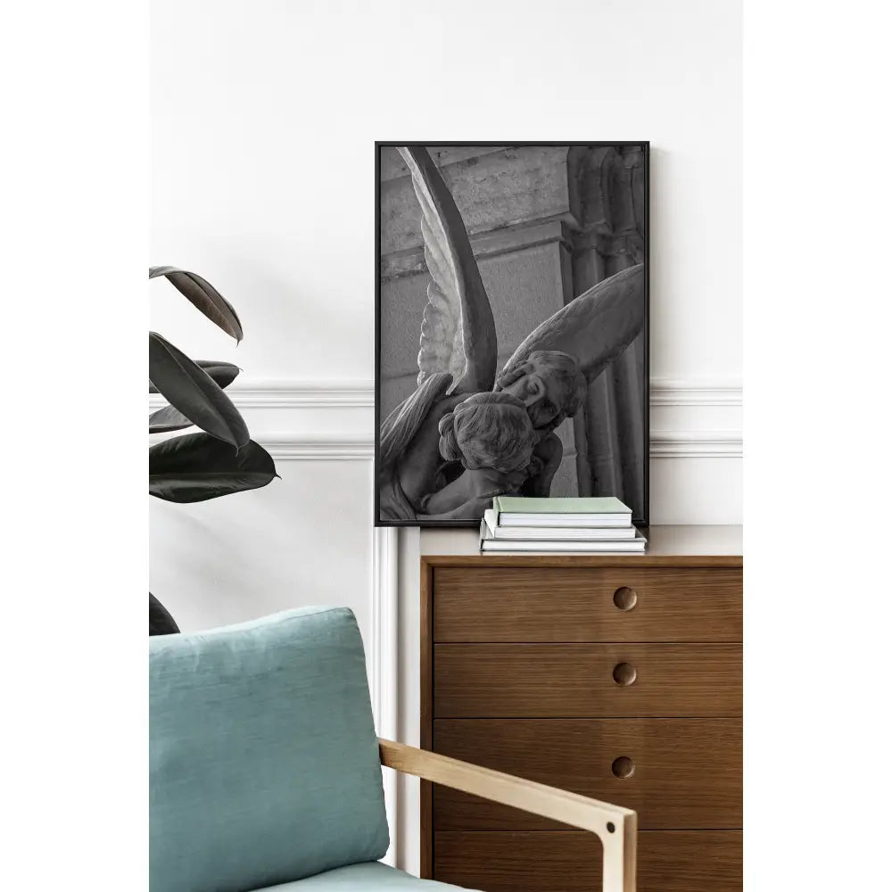 Framed black and white artwork of a cherub on a wall above a wooden dresser with books.