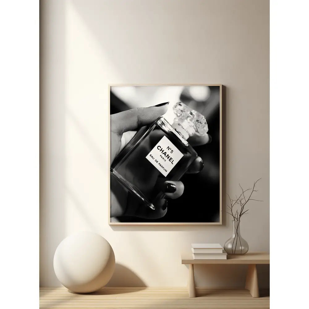 Framed artwork of a hand holding a Chanel perfume bottle on a wall in a modern interior setting.